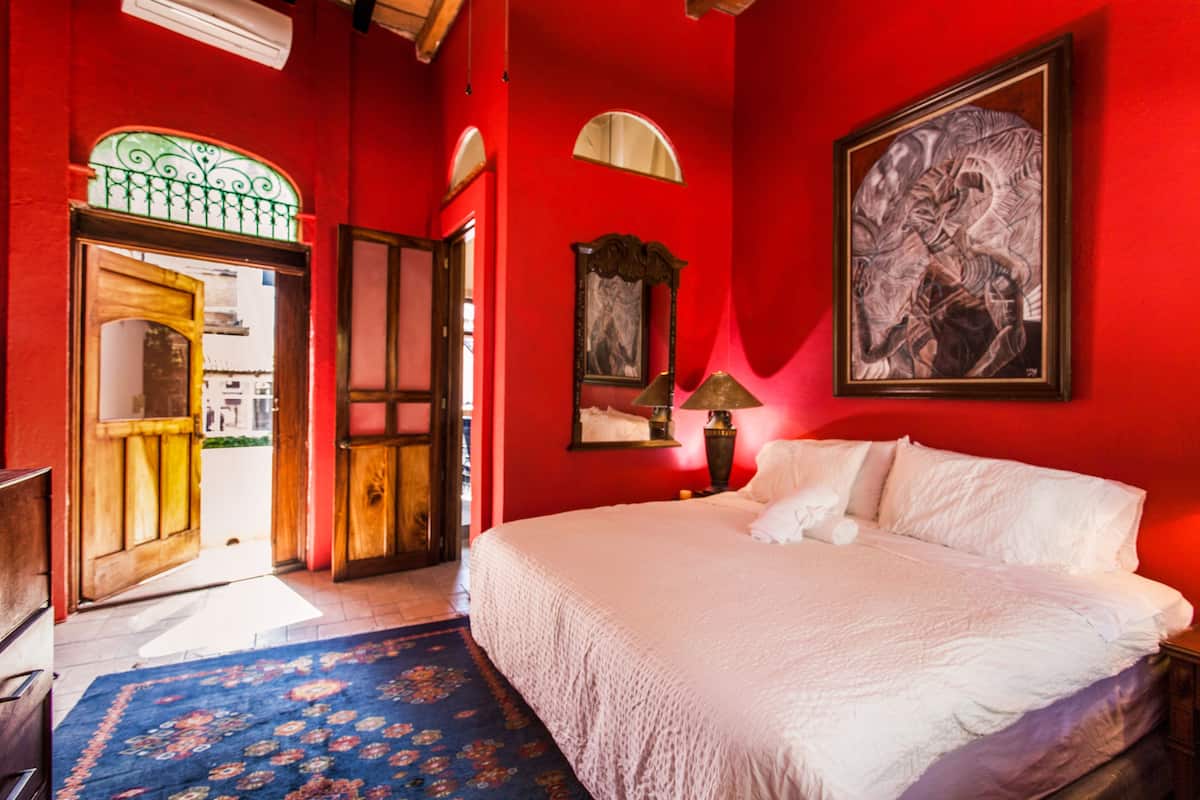 Una habitación con una cama grande, una puerta que da al exterior, un cuadro en la pared y una lámpara.