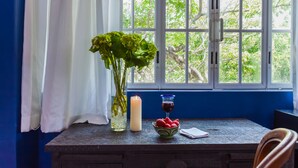 A window with a view of trees, a candle, a glass of red wine, and a bowl of strawberries on a table. - Garlands del Rio Riverside Boutique Hotel (Puerto Vallarta)