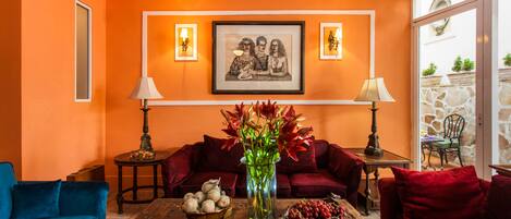 A living room with orange walls, a framed picture, two lamps, a vase with flowers, a coffee table with decorative items, and red and blue sofas.