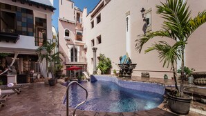 A swimming pool with stone flooring, surrounded by potted plants and a red umbrella. - Garlands del Rio Riverside Boutique Hotel (Puerto Vallarta)