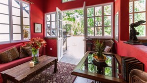 A room with a red wall, a wooden coffee table, a sofa with leopard print cushions, a glass-top table with fruit, and a statue on the wall. - Garlands del Rio Riverside Boutique Hotel (Puerto Vallarta)