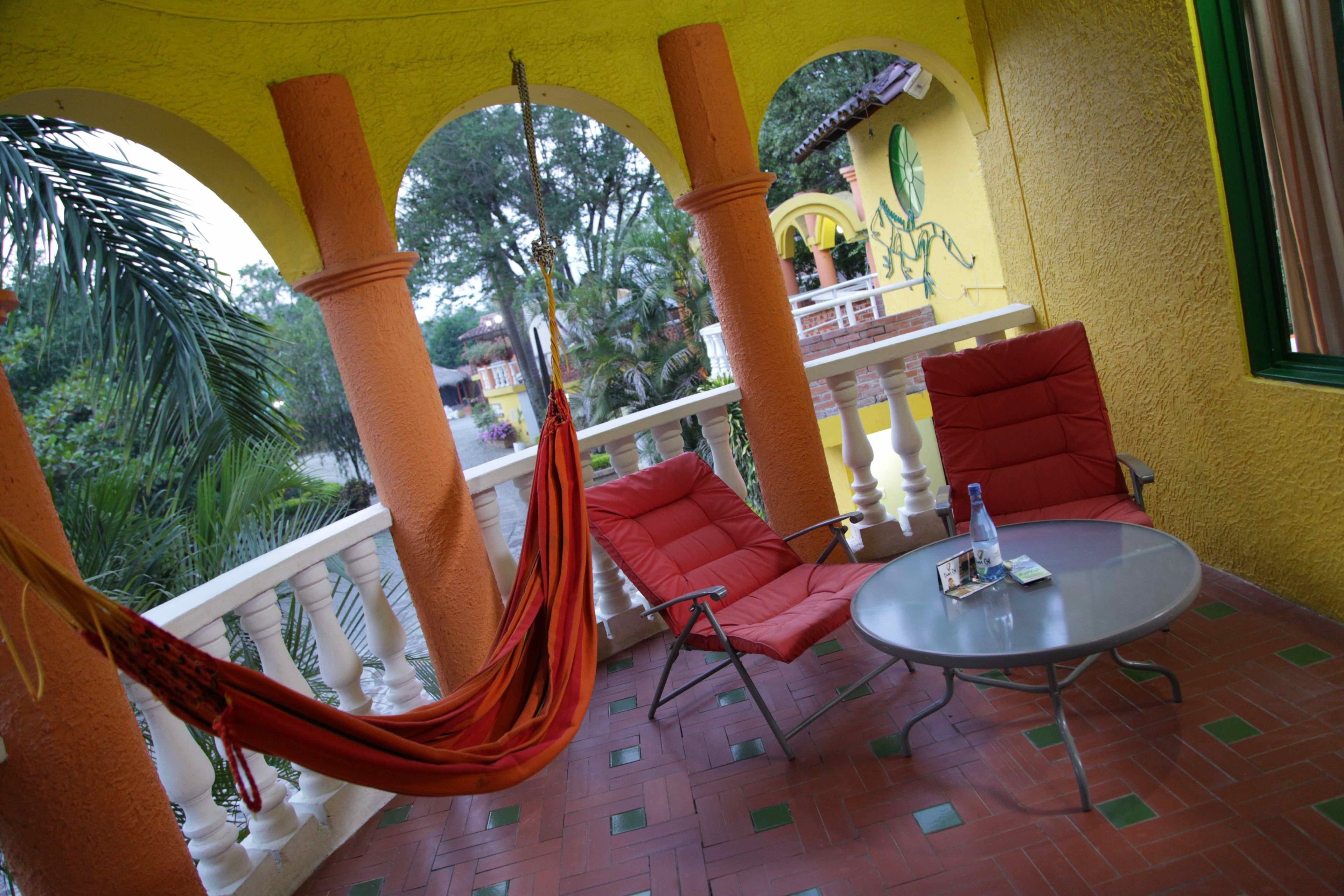 A balcony with red chairs, a hammock, and a table with a bottle and a card.