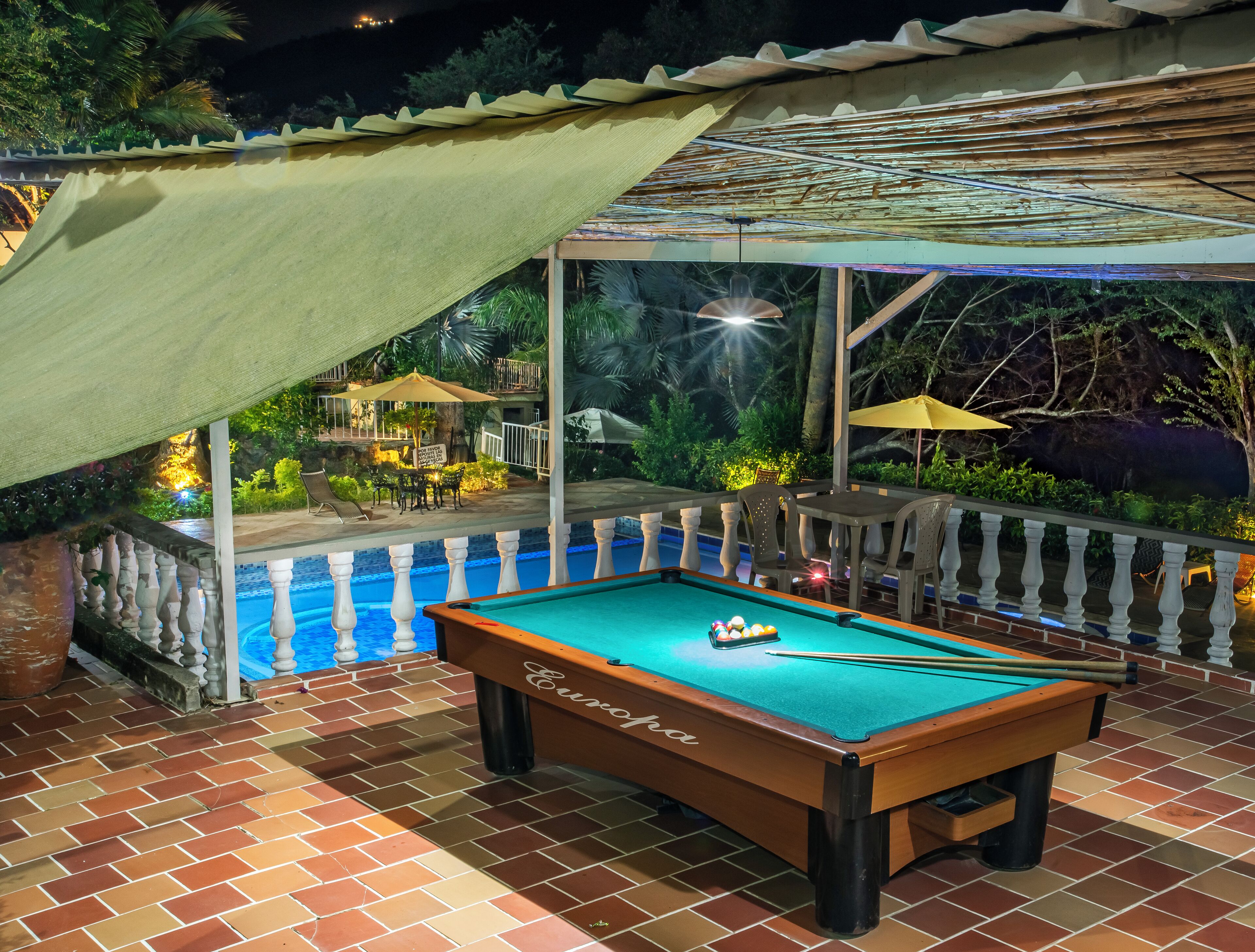 A pool table with a green felt surface, surrounded by a tiled patio area with a brick pattern.