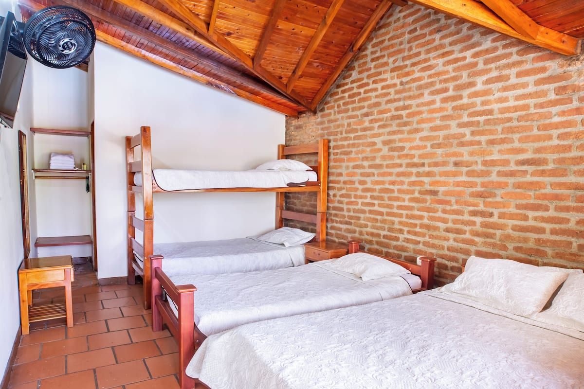 A room with two bunk beds, a wooden ceiling, a brick wall, and a small table with a fan.
