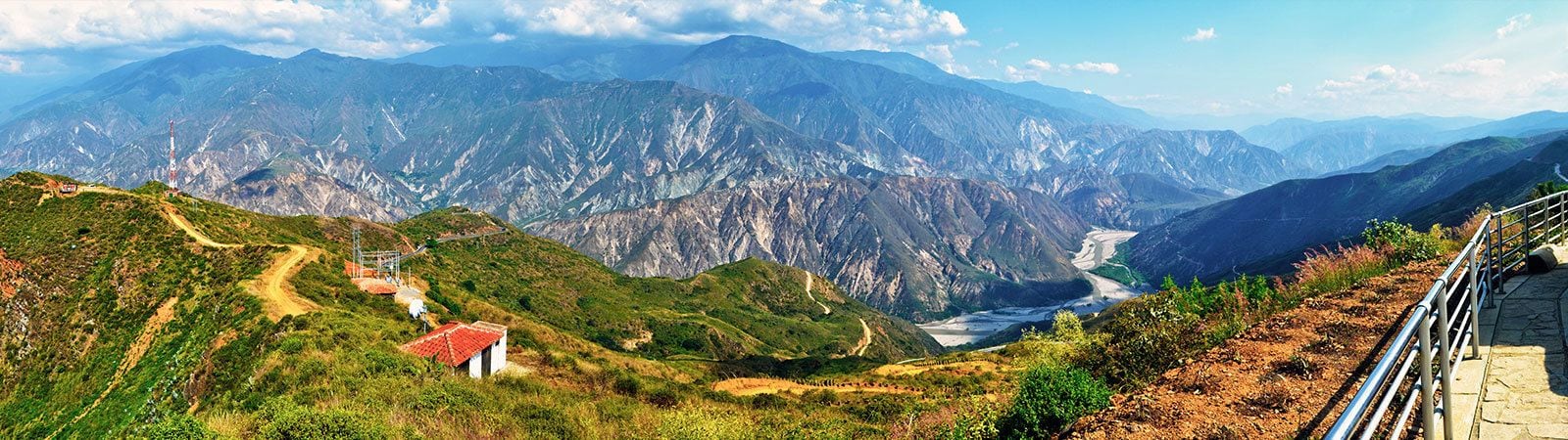 A mountainous landscape with a river, a small building, and a paved path.