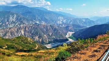A mountainous landscape with a river, a small building, and a paved path.