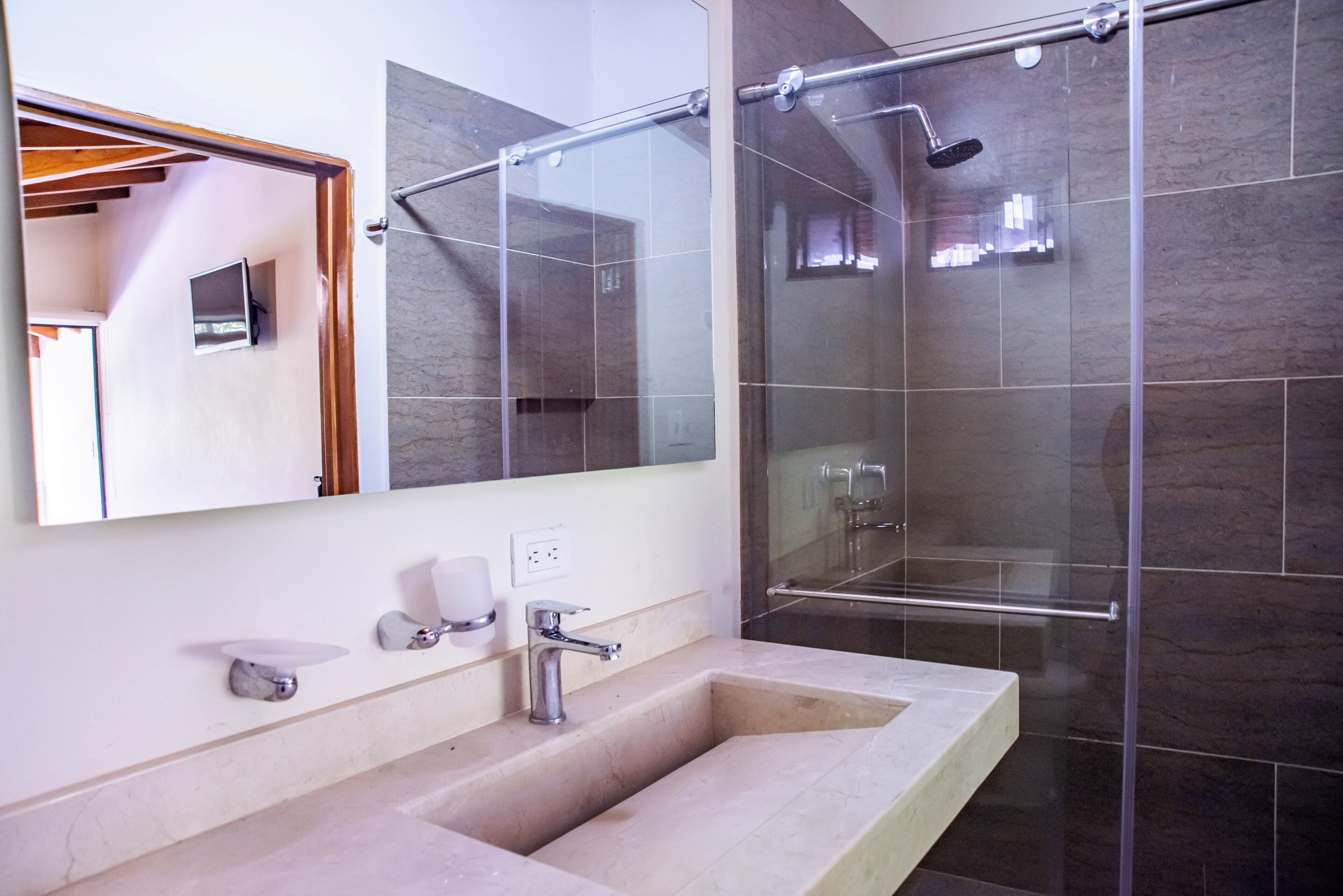 A modern bathroom with a large mirror, a sink, and a glass-enclosed shower.