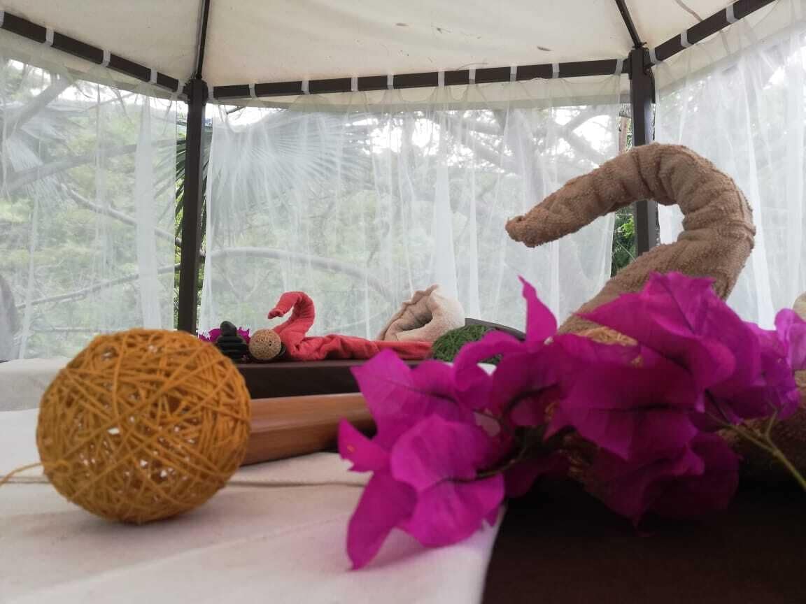 A tent with a table inside, featuring a ball of yarn, a stuffed flamingo, a stuffed giraffe, and purple flowers.