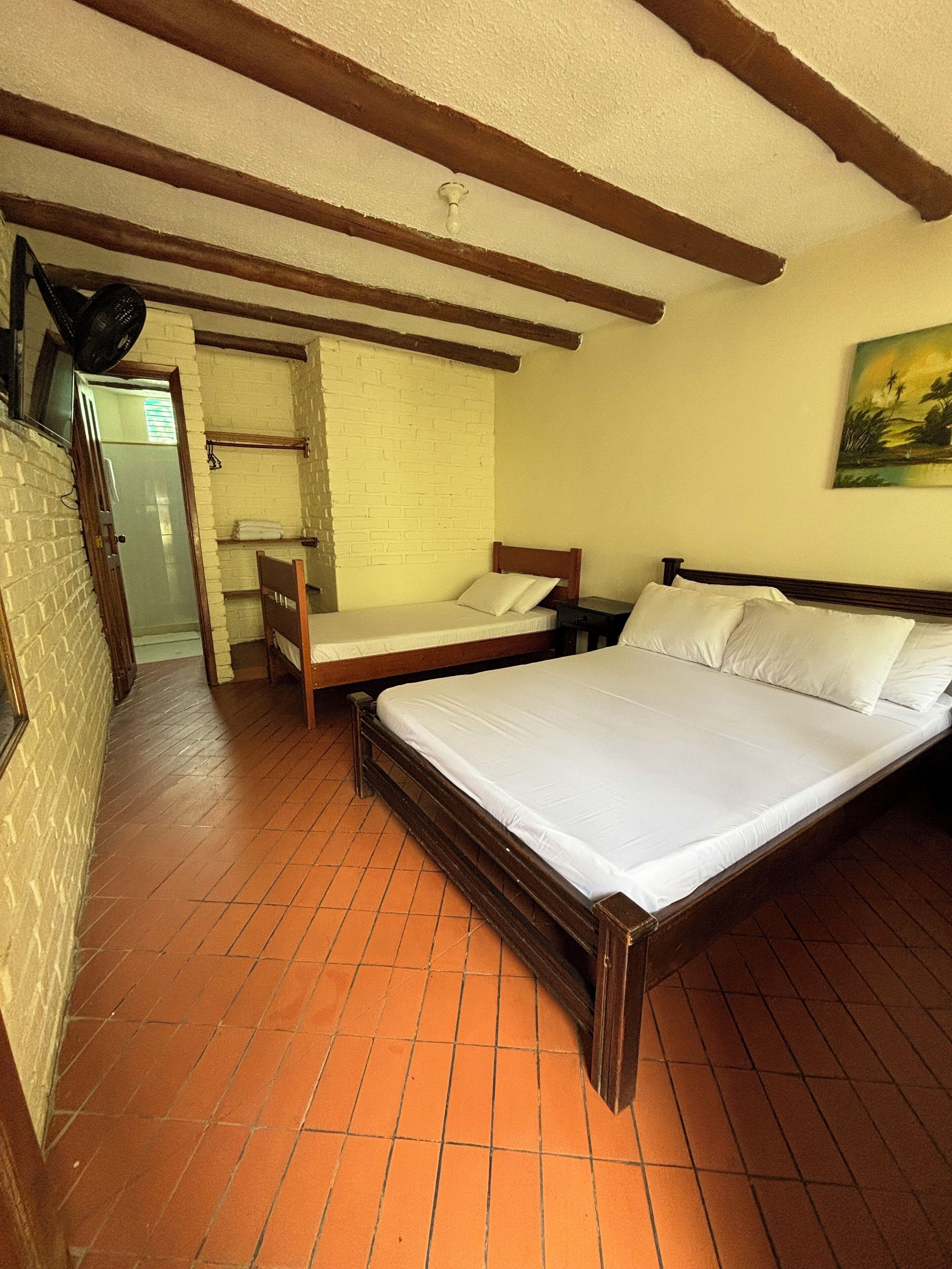 A bedroom with two single beds, a wooden headboard, a brick wall, and a tiled floor.