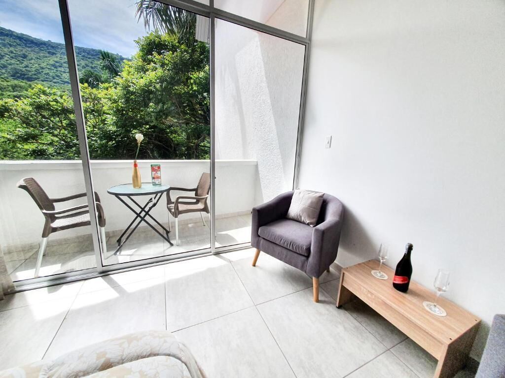 Een balkon met uitzicht op weelderige begroeiing, een zithoek met een stoel en een klein tafeltje, en een fles wijn op een houten bijzettafeltje.