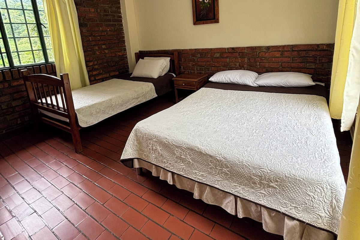A room with two single beds, a wooden chair, and a brick wall.