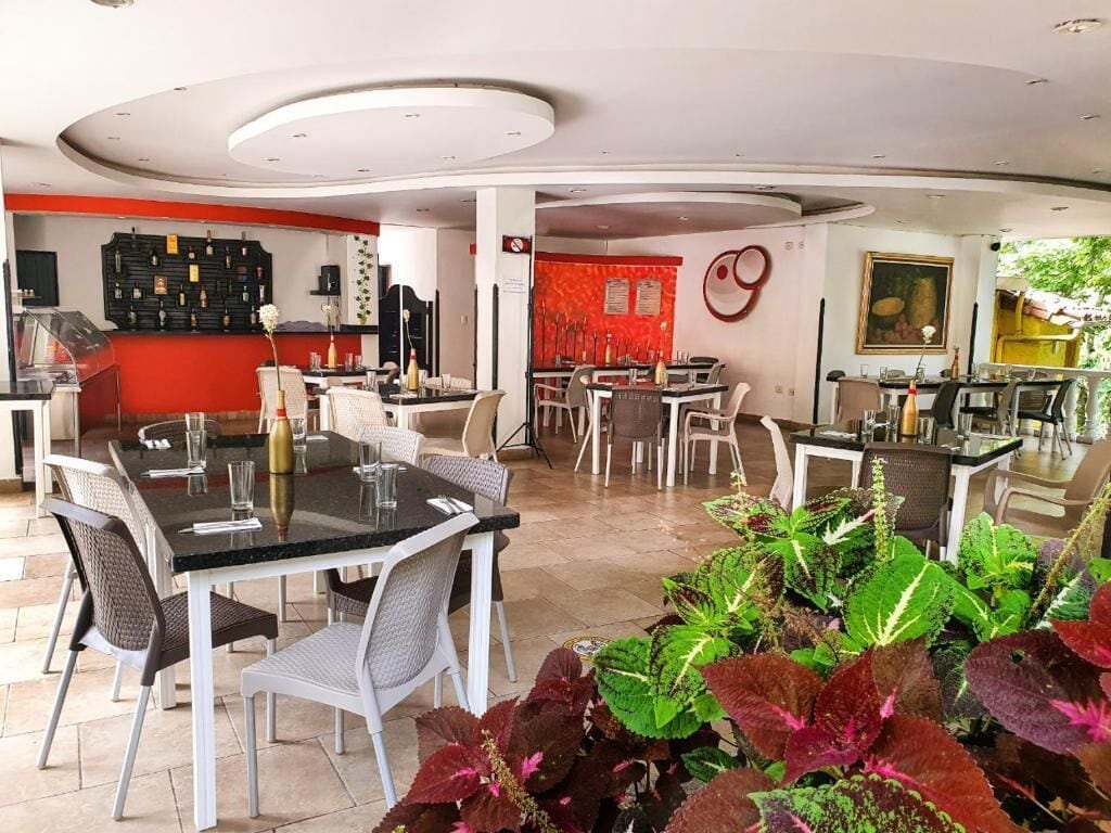 Un ristorante con diversi tavoli e sedie, una zona bar e una varietà di piante sullo sfondo.