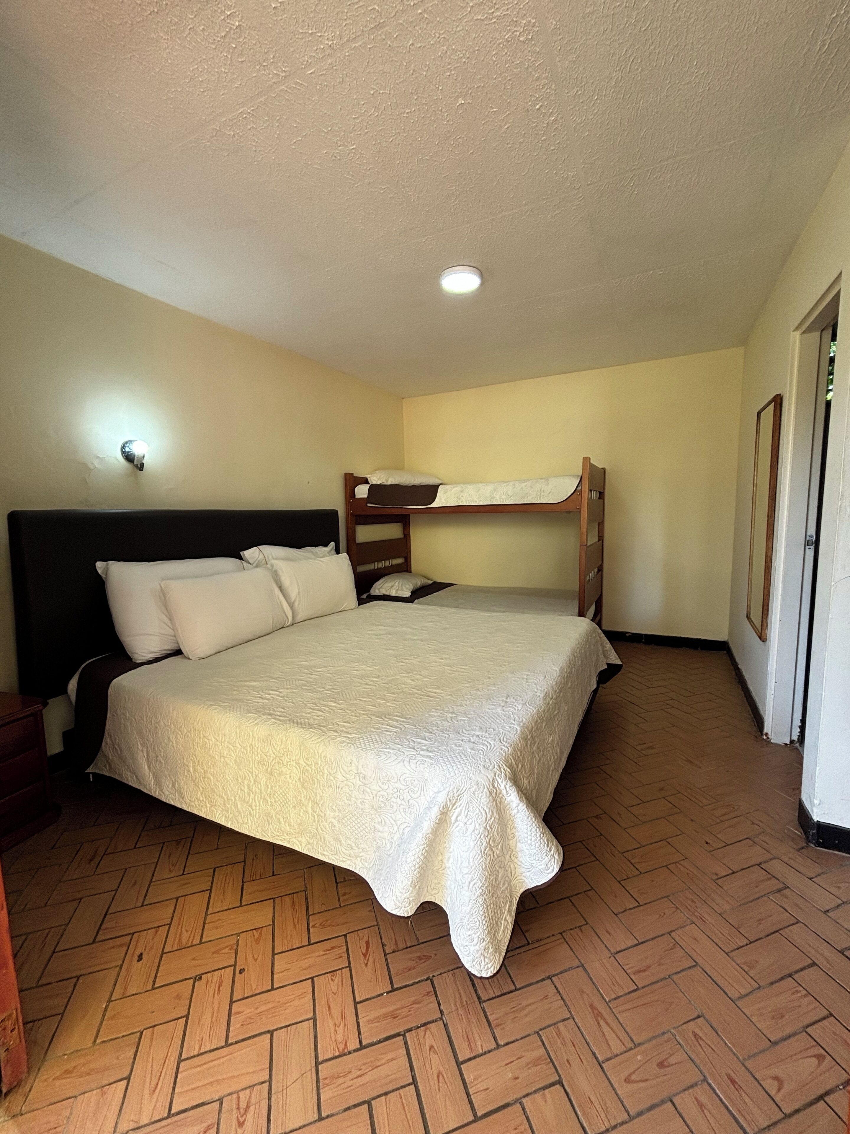 A bedroom with a large bed, a smaller bunk bed, a wooden dresser, and a nightstand.