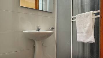 Un baño con lavabo pedestal, inodoro, espejo y ducha con una toalla colgada en la puerta.