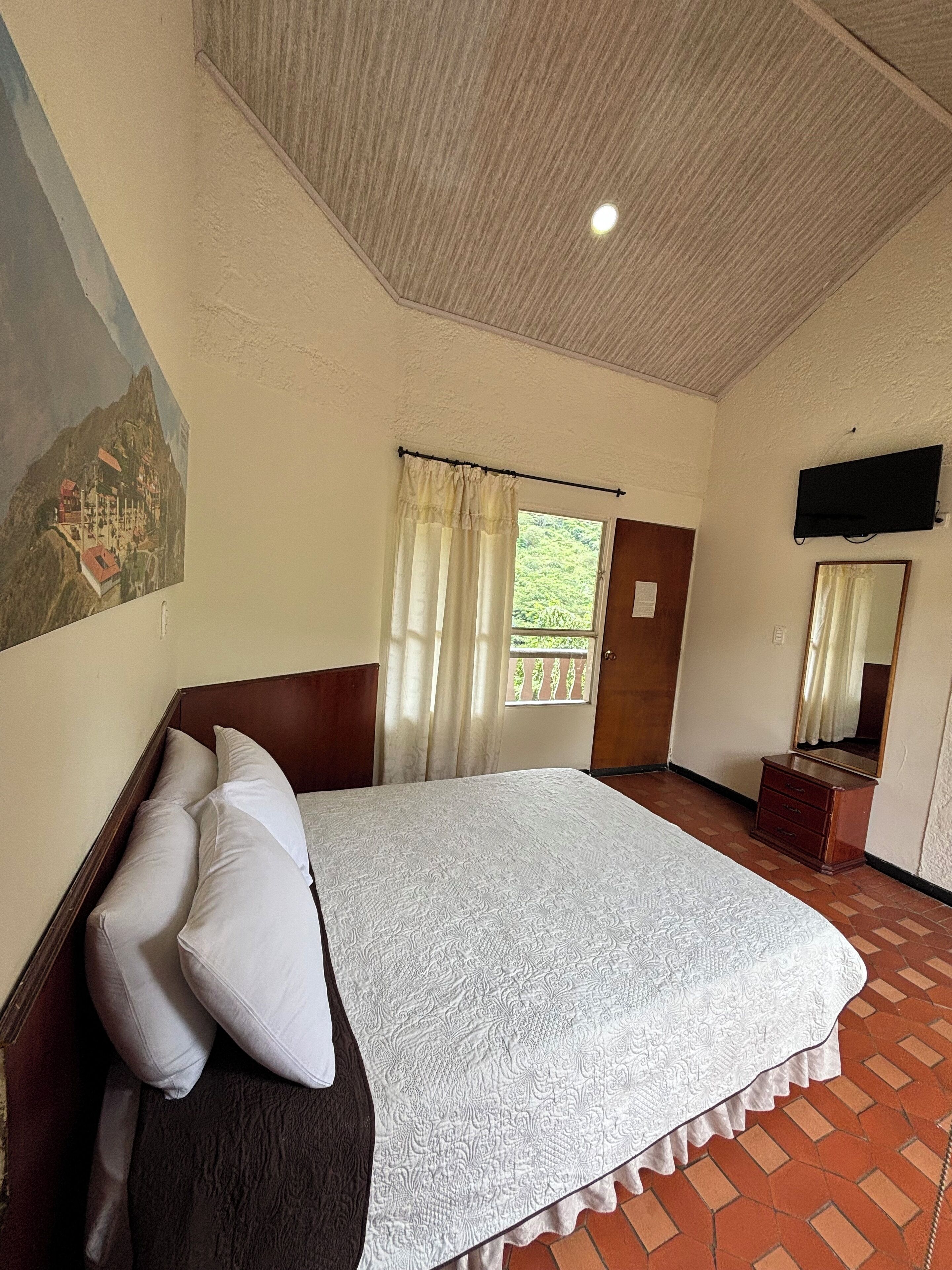 Un dormitorio con una cama grande, cabecera de madera, televisión de pantalla plana, un espejo y una puerta que da a un balcón.