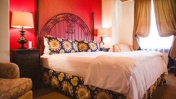 A hotel room with a large bed, two bedside tables with lamps, a red accent wall, and a window with curtains.