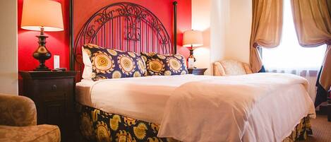 A hotel room with a large bed, two bedside tables with lamps, a red accent wall, and a window with curtains.