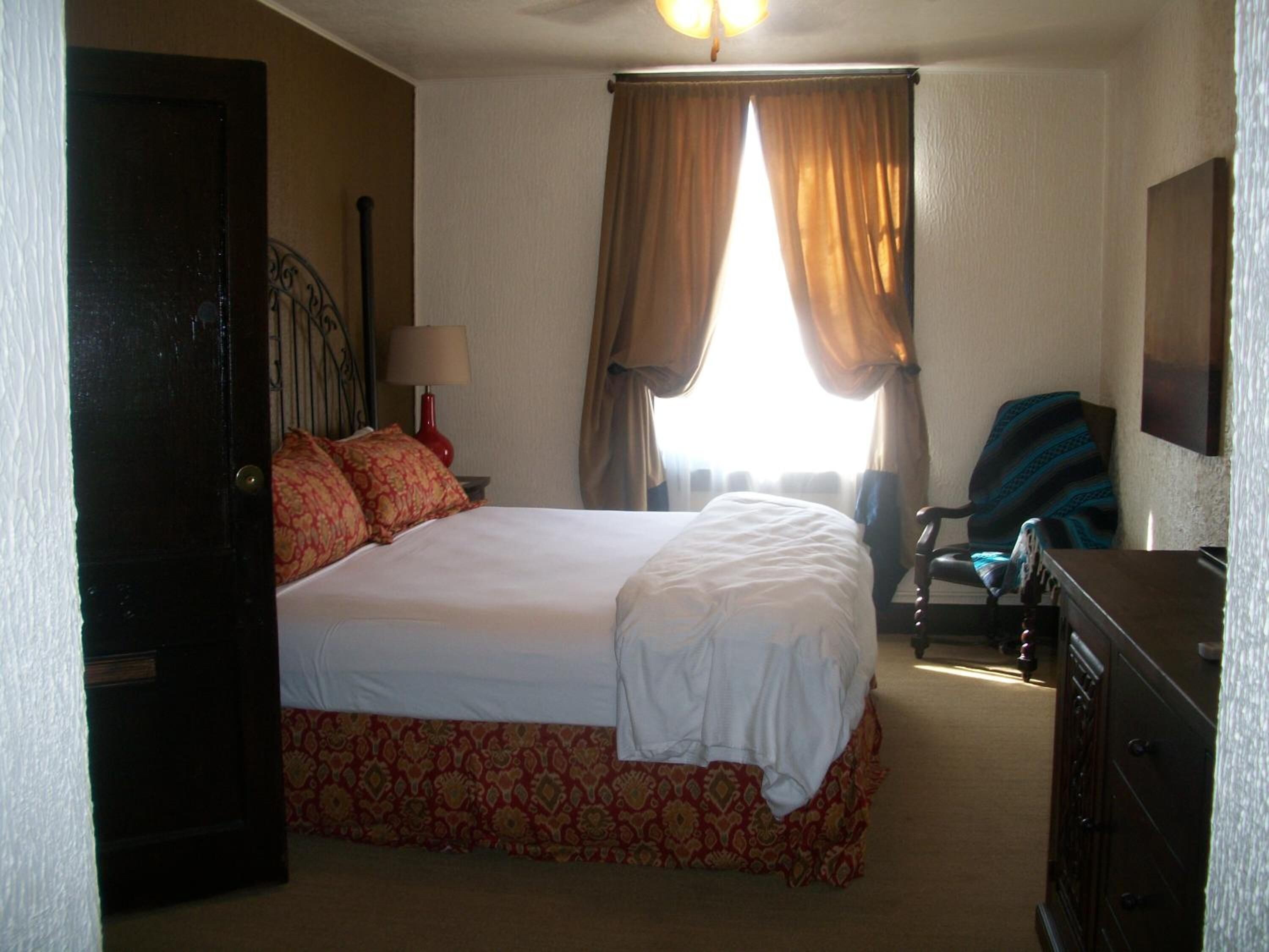 Una habitación de hotel con una cama, una silla, una lámpara y una ventana con cortinas.