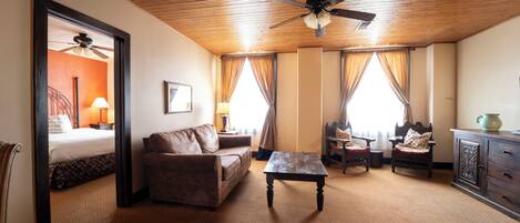 Une chambre d’hôtel avec un plafond en bois, un lit, un canapé, une table basse, une chaise, une armoire et une fenêtre avec des rideaux.