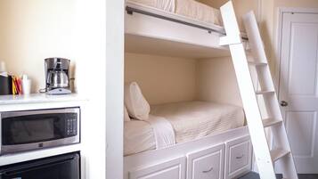 Een stapelbed met een ladder, een magnetron, een koffiezetapparaat en een koelkast in een kamer met een deur en een vloerbedekking.
