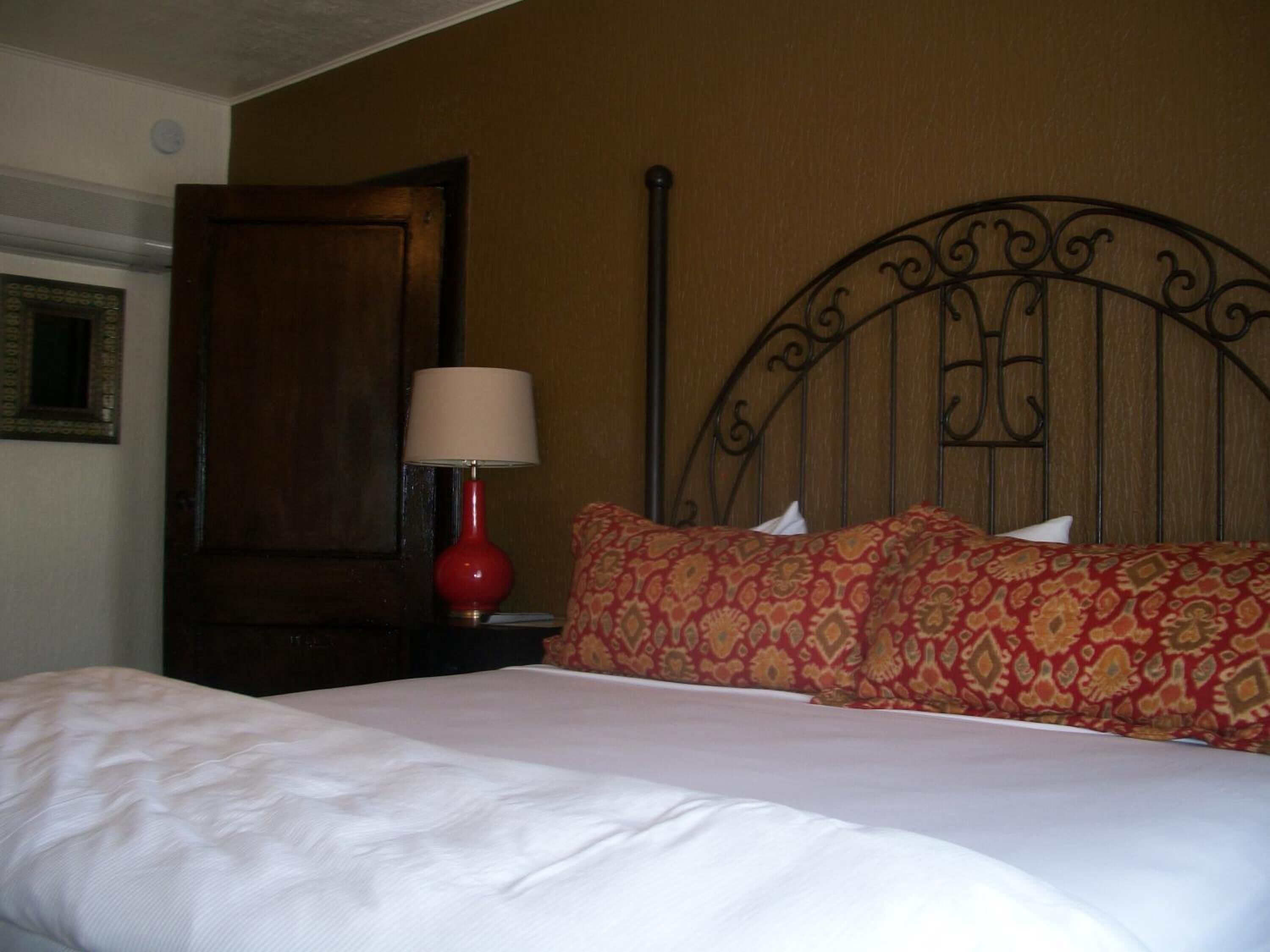 A neatly made bed with a patterned pillow and a red lamp beside it.