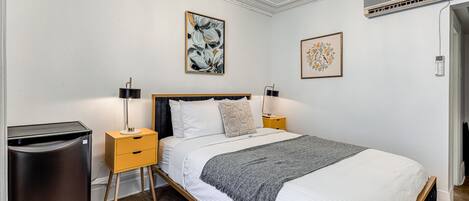 A bedroom with a bed, bedside tables, a lamp, a heater, and artwork on the walls.
