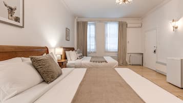 A hotel room with two beds, a chandelier, a radiator, and a framed picture on the wall.