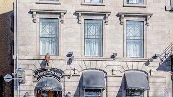 Un edificio de dos pisos con entrada a nivel de calle, un letrero sobre la puerta y un pequeño toldo sobre la entrada.