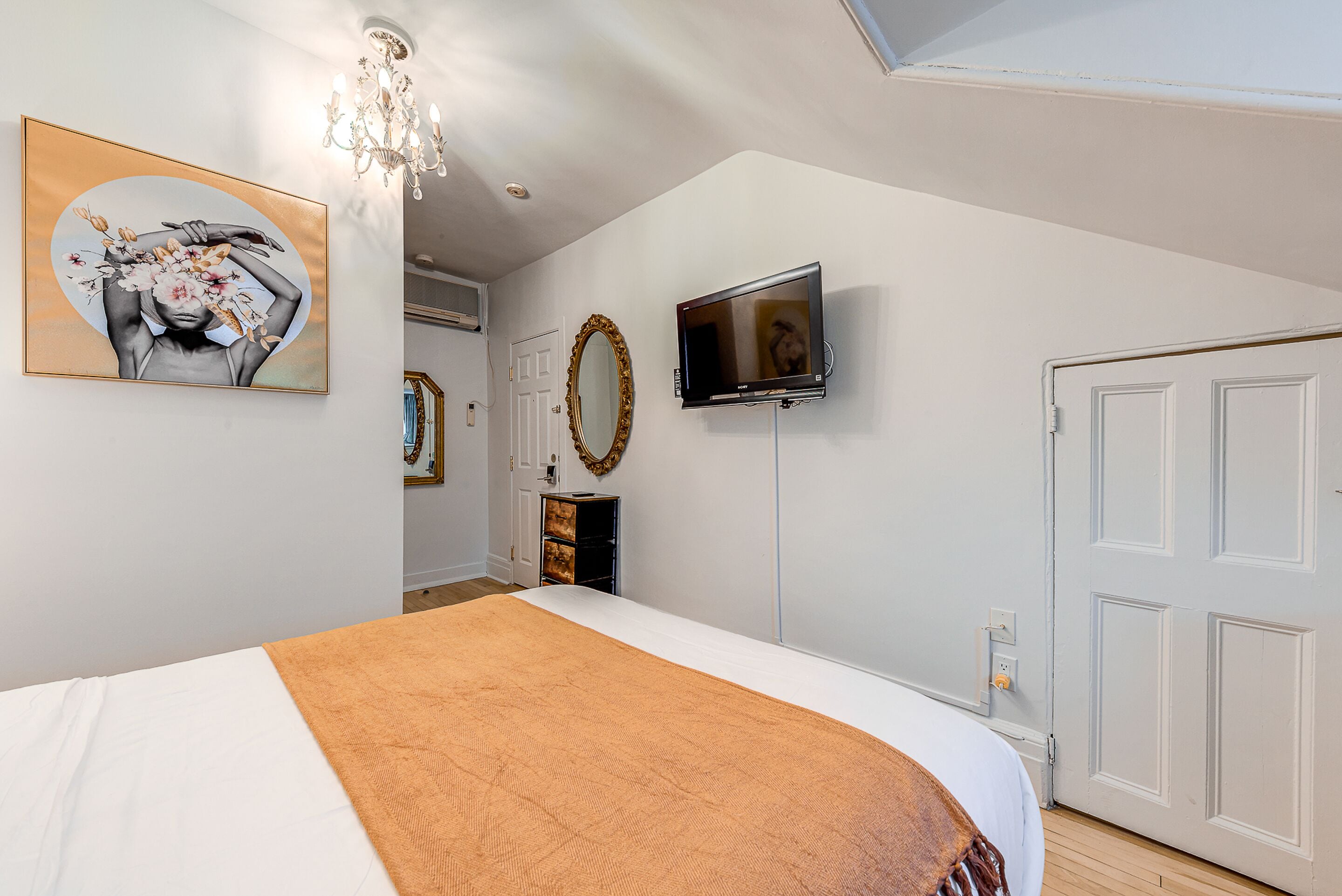 A bedroom with a large bed, a television, a chandelier, and a painting on the wall.