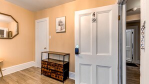 A hallway with a wooden floor, a white door with a '4' sign, a small table with drawers, and a mirror on the wall. - North House - Auberge la chouette / Hôtel Automatisé (Québec City)