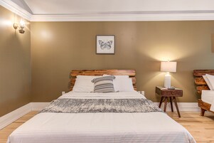 Un dormitorio con cama, mesita de noche, lámpara y un cuadro con una mariposa en la pared.