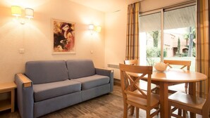 Une pièce avec un canapé bleu, une table à manger en bois et des chaises, un tableau accroché au mur et une fenêtre avec des rideaux.