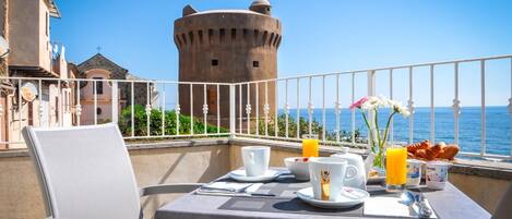 Een balkon met een ontbijtje, met uitzicht op een historische toren en de zee.