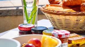 A breakfast setting with flowers, croissants, and condiments by a window overlooking the sea.