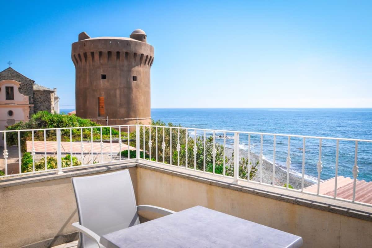 Ein Balkon mit Tisch und Stühlen mit Blick auf das Meer und einen historischen Turm.