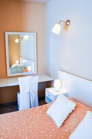 Habitación de hotel con cama, escritorio con lámpara, silla, espejo y una lámpara de pared.