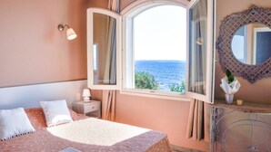 A bedroom with a bed, a nightstand, a mirror, and a window with a view of the sea.