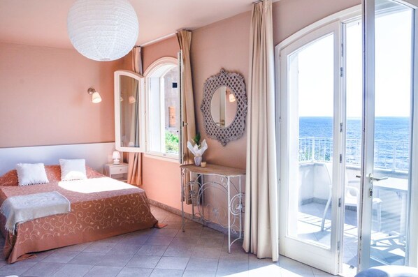 A bedroom with a bed, a vanity with a mirror, and a balcony with a view of the sea. - Hôtel restaurant le Torremare (Santa-Maria-di-Lota)