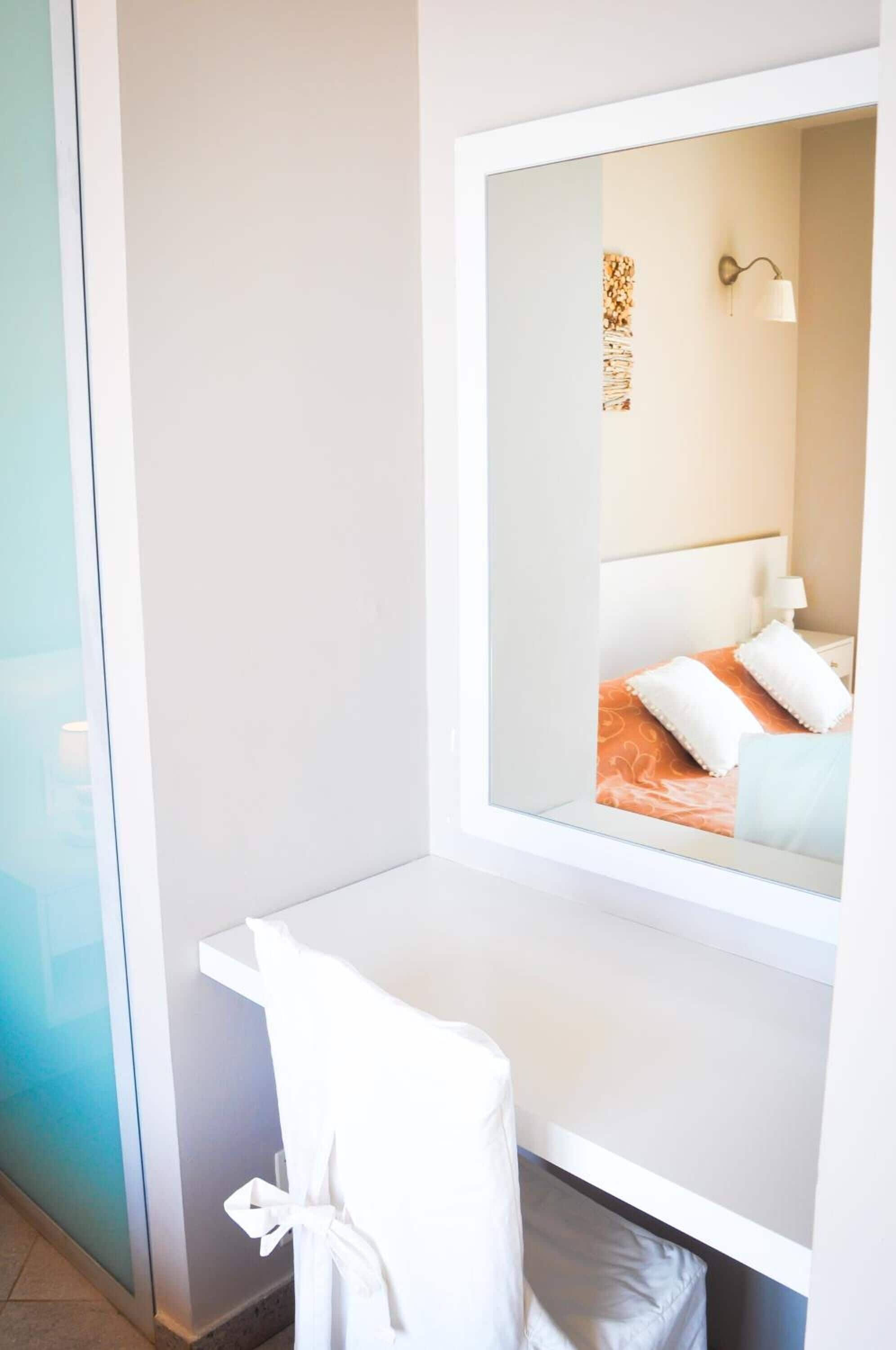 A modern hotel room with a large mirror, a white desk, and a chair.