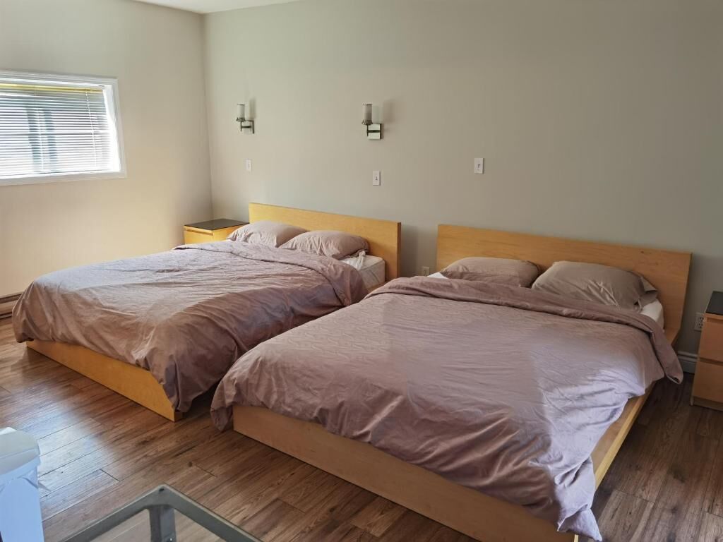 A room with two beds, a window with blinds, and two wall-mounted nightstands.