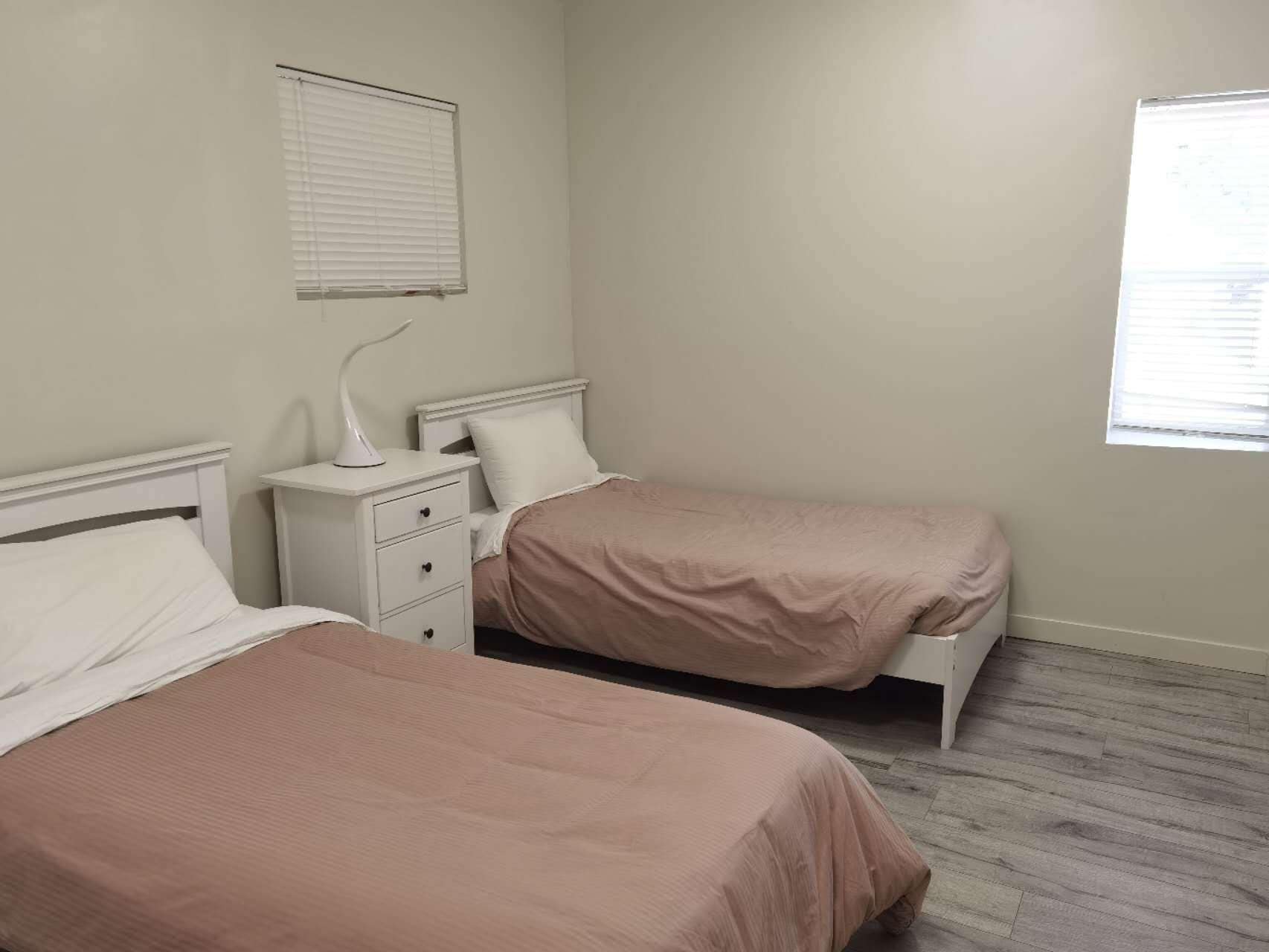 A bedroom with two beds, a nightstand, and a window with blinds.