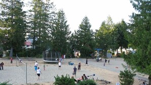 Un espacio recreativo al aire libre con una red de voleibol, un trampolín y bicicletas estacionadas cerca.