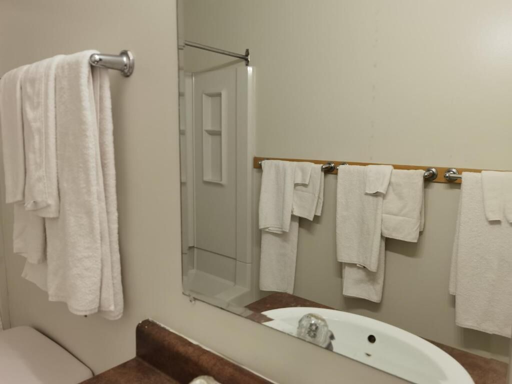 A bathroom with a white sink, a mirror, and multiple white towels hanging on a rack.