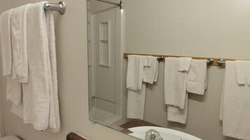 A bathroom with a white sink, a mirror, and multiple white towels hanging on a rack.