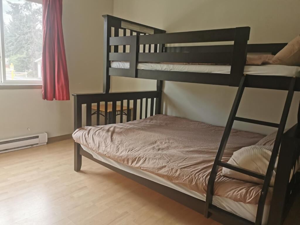 Ein Etagenbett mit Kopfteil und Fußteil, ein Fenster mit rotem Vorhang und ein Heizkörper am Boden.