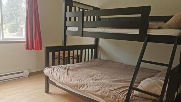 A bunk bed with a headboard and footboard, a window with a red curtain, and a radiator on the floor. - Qualicum Bay Resort (Qualicum Beach)