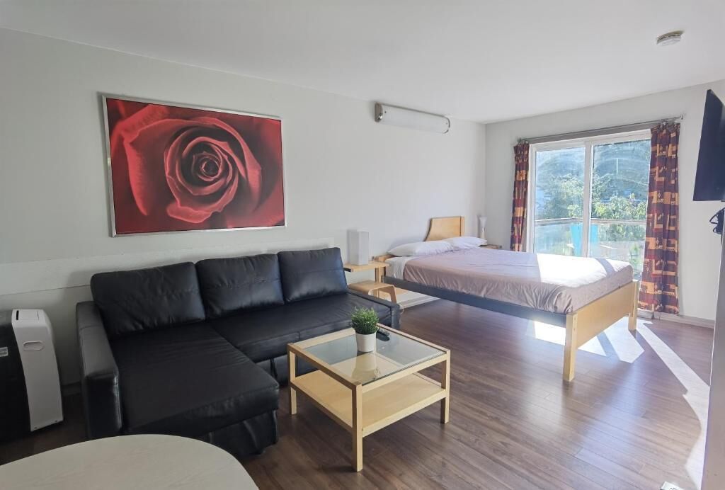 A modern room with a bed, a sofa, a glass coffee table, and a large window with curtains.