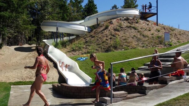 Un tobogán de agua en un parque con una zona de césped y árboles al fondo.