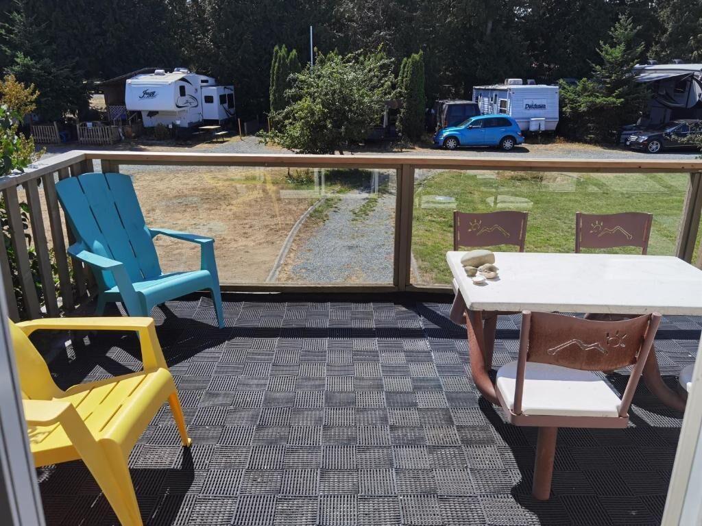 A balcony with a table and chairs, a view of a grassy area, and RVs in the background.