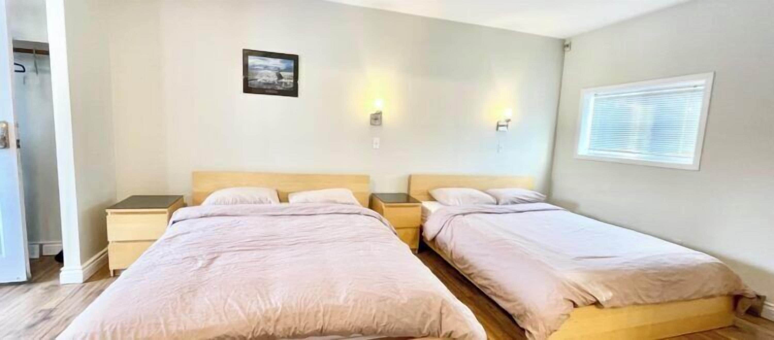 Una habitación con dos camas, una mesita de noche pequeña, un cuadro colgado en la pared y una ventana con persianas.